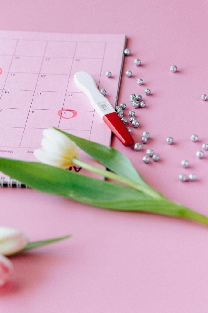 A pregnancy test, tulips, and calendar on pink backdrop conveying anticipation.
