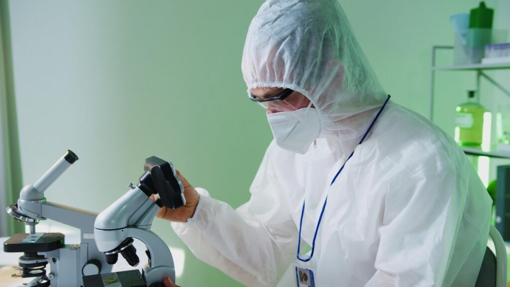 pexels photo 8533040 8533040 A scientist in protective gear examines samples under a microscope in a lab.