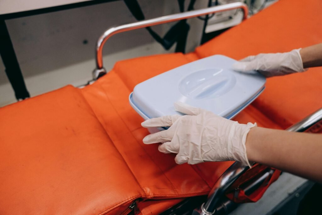pexels photo 8943341 8943341 Focused shot of gloved hands handling a first aid kit on an orange stretcher in a medical setting.